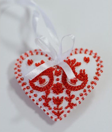 Decorative heart ornament with red bead patterns and a white ribbon on a light gray background