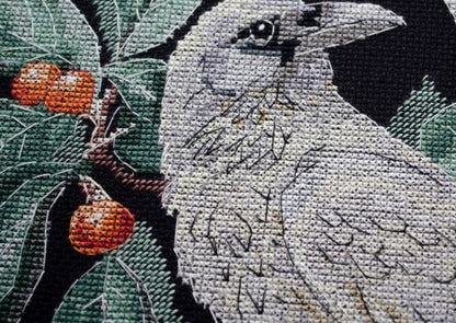Cross-stitched crow with leaves and berries on fabric