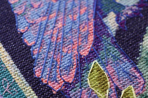 Close-up of cross stitch with floral embroidery in pink, purple, and green.