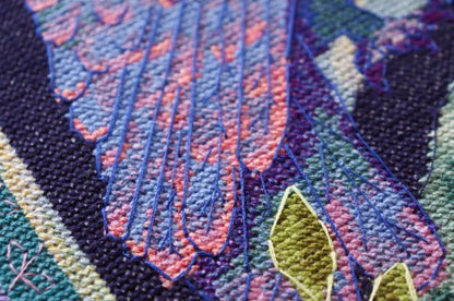 Close-up of cross stitch with floral embroidery in pink, purple, and green.
