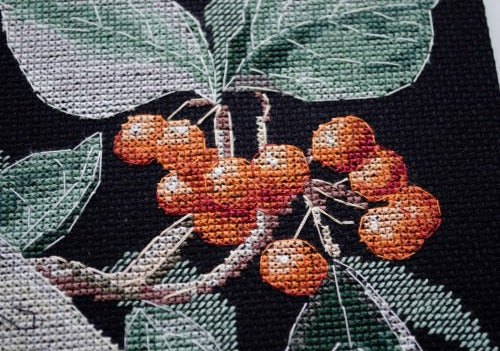 Cross-stitched design of berries and leaves on black fabric